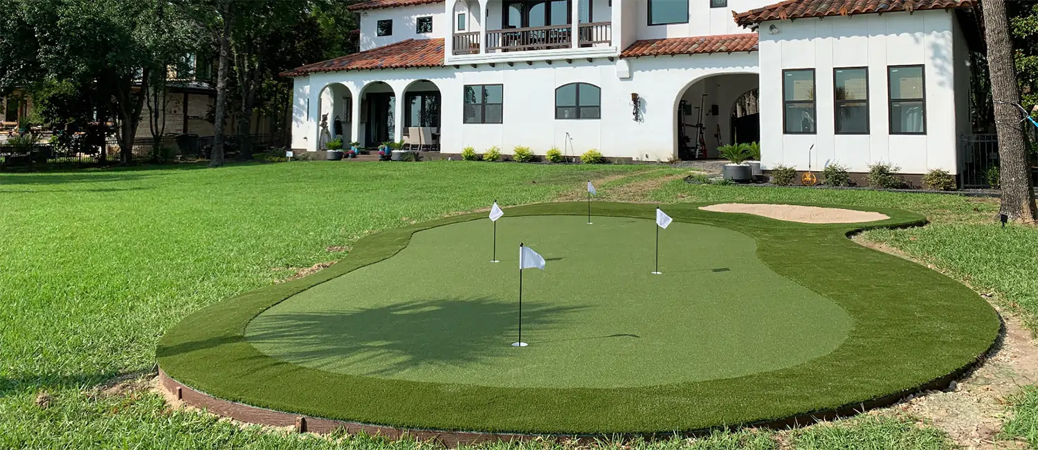 Backyard putting green next to white residential house installed by SYNLawn